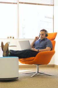 man wearing headphones sitting on orange padded chair while using laptop computer